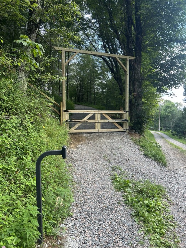 Custom wood farm gate with gooseneck post across a gravel drive by Mountain Fence and Deck